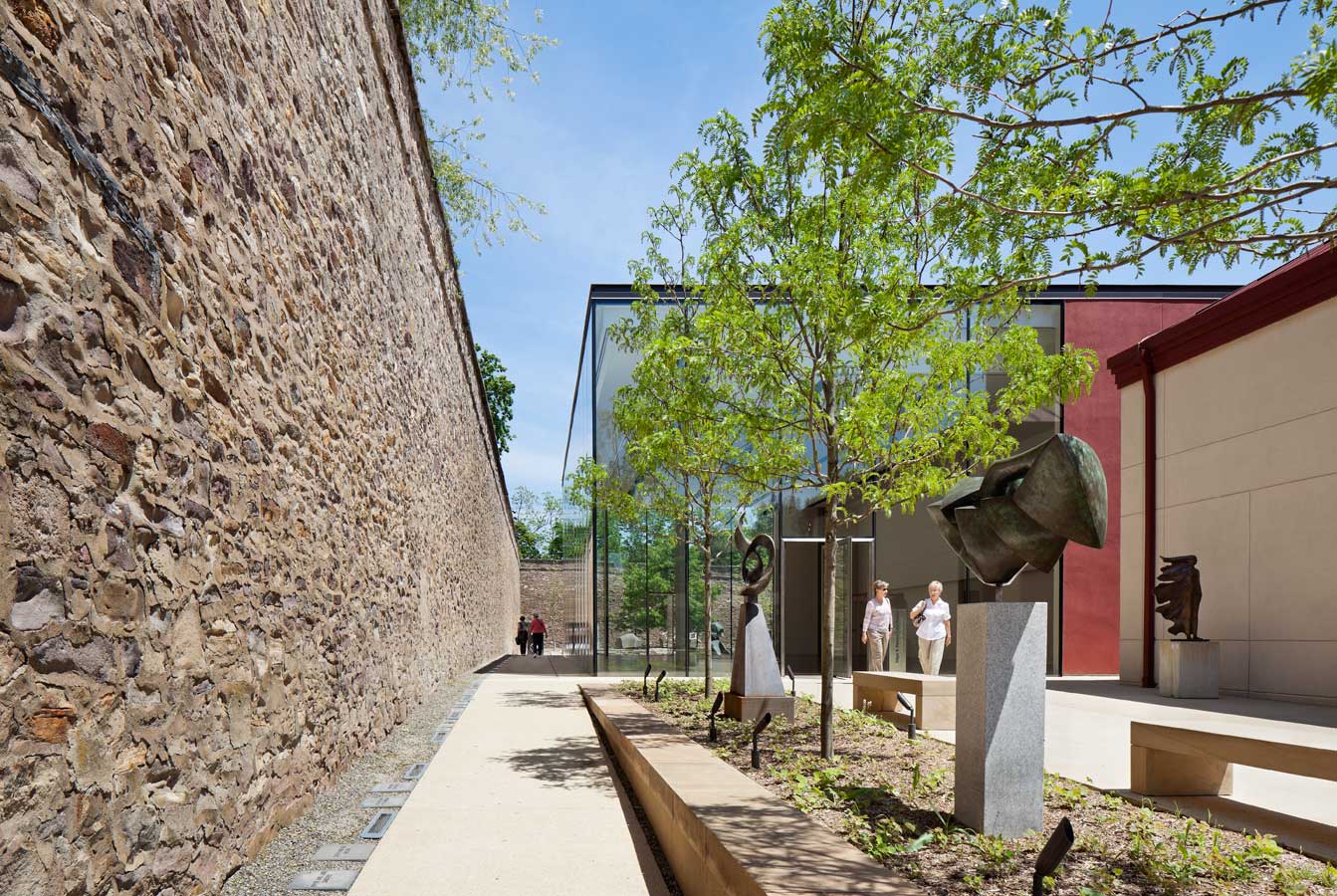 <p>The stone wall of the former prison appears to enter the space through the uninterrupted glass walls of the pavilion, lending visual interest and historical reference to the structure. <br><small>&copy; Michael Moran/OTTO</small></p>